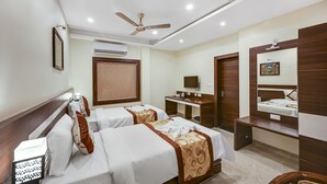 A hotel room with two beds, a desk, a mirror, and a ceiling fan.