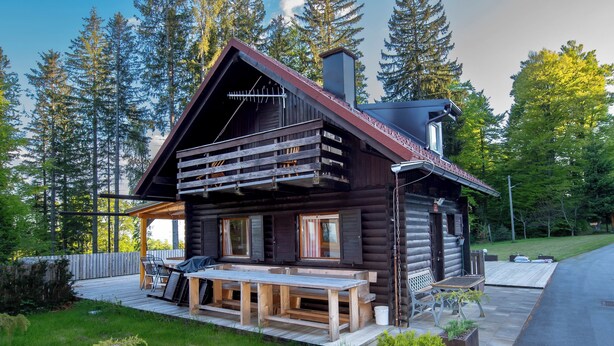Une cabane en rondins avec une terrasse, un espace salon extérieur et une cheminée.