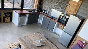 A modern kitchen with a wooden table and bench, stone wall, and built-in appliances.
