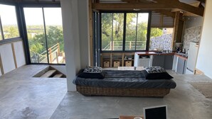 A modern room with a large bed, a laptop on a wooden table, and a view of a balcony with a railing.