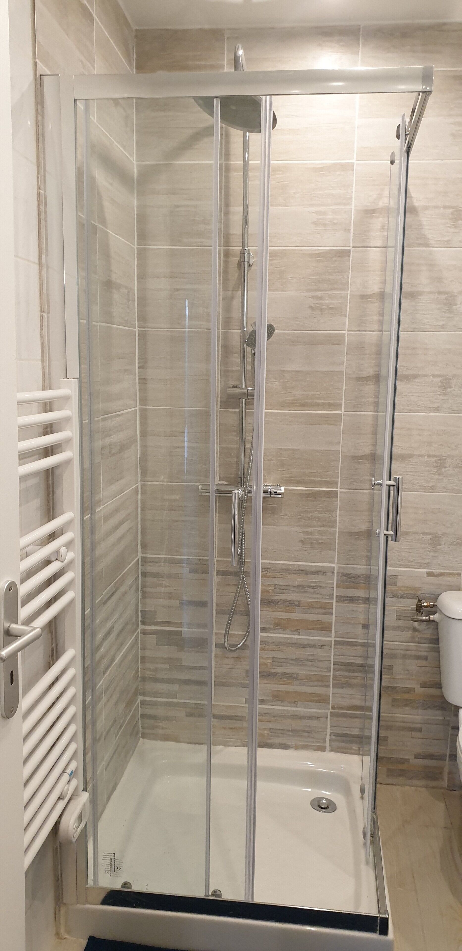 A glass-enclosed shower stall with a white bathtub, tiled walls, and a white toilet visible to the right.