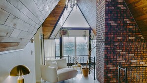 Ein Schlafzimmer im Loft-Stil mit schrägverdeckter Decke, einem weißen Sofa, einem Bett und Bergblick durch große Fenster.