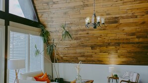 Ein gemütliches Wohnzimmer im Loft-Stil mit schräg versiegelter Decke, Holzpaneelen, einem Chandelier und einer Mischung aus modernen und klassischen Möbeln.