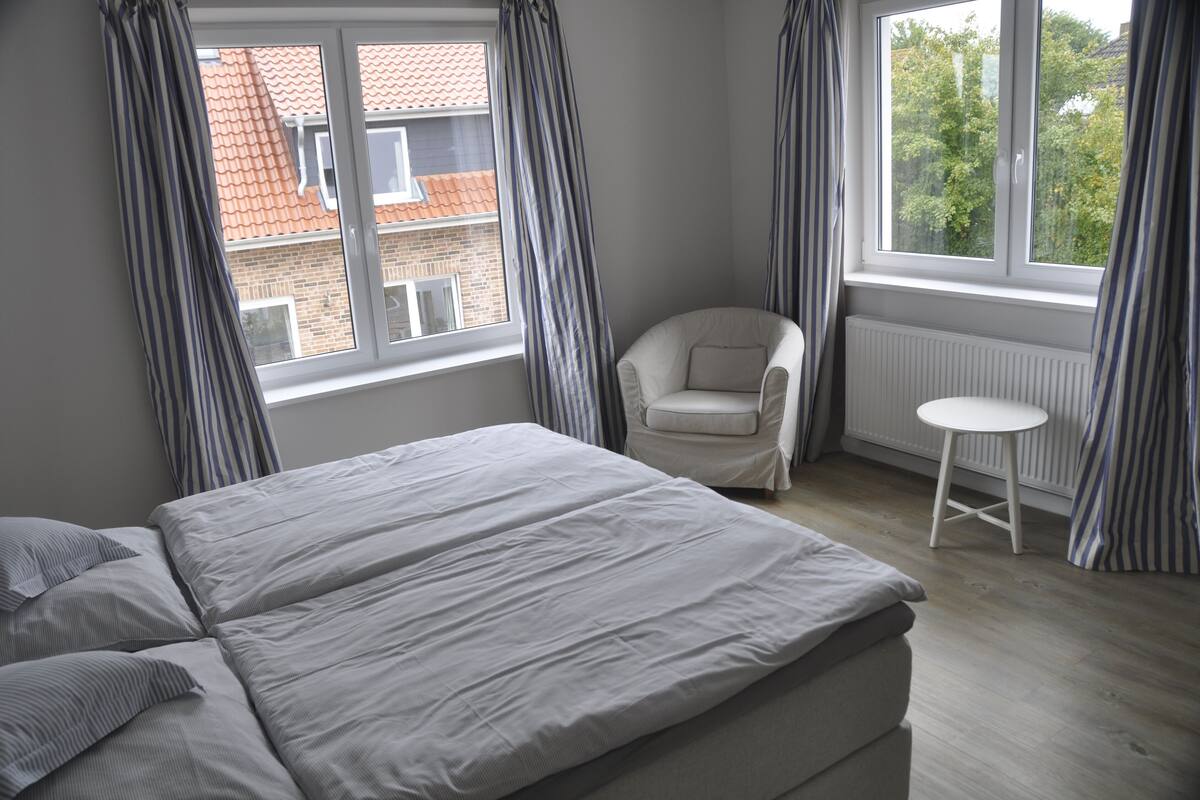 Une chambre à coucher avec un lit, une chaise, une petite table et une fenêtre avec des rideaux.