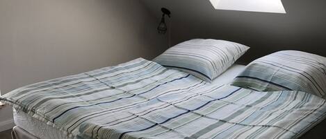 A bedroom with a skylight, a bed with striped bedding, and a small wall-mounted light fixture.