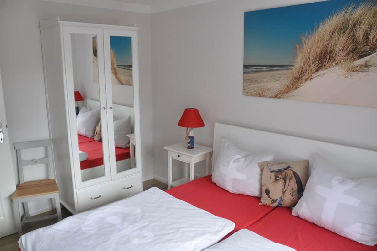 Une chambre à coucher comprenant un lit, une armoire, une table de chevet et un tableau représentant une scène de plage.