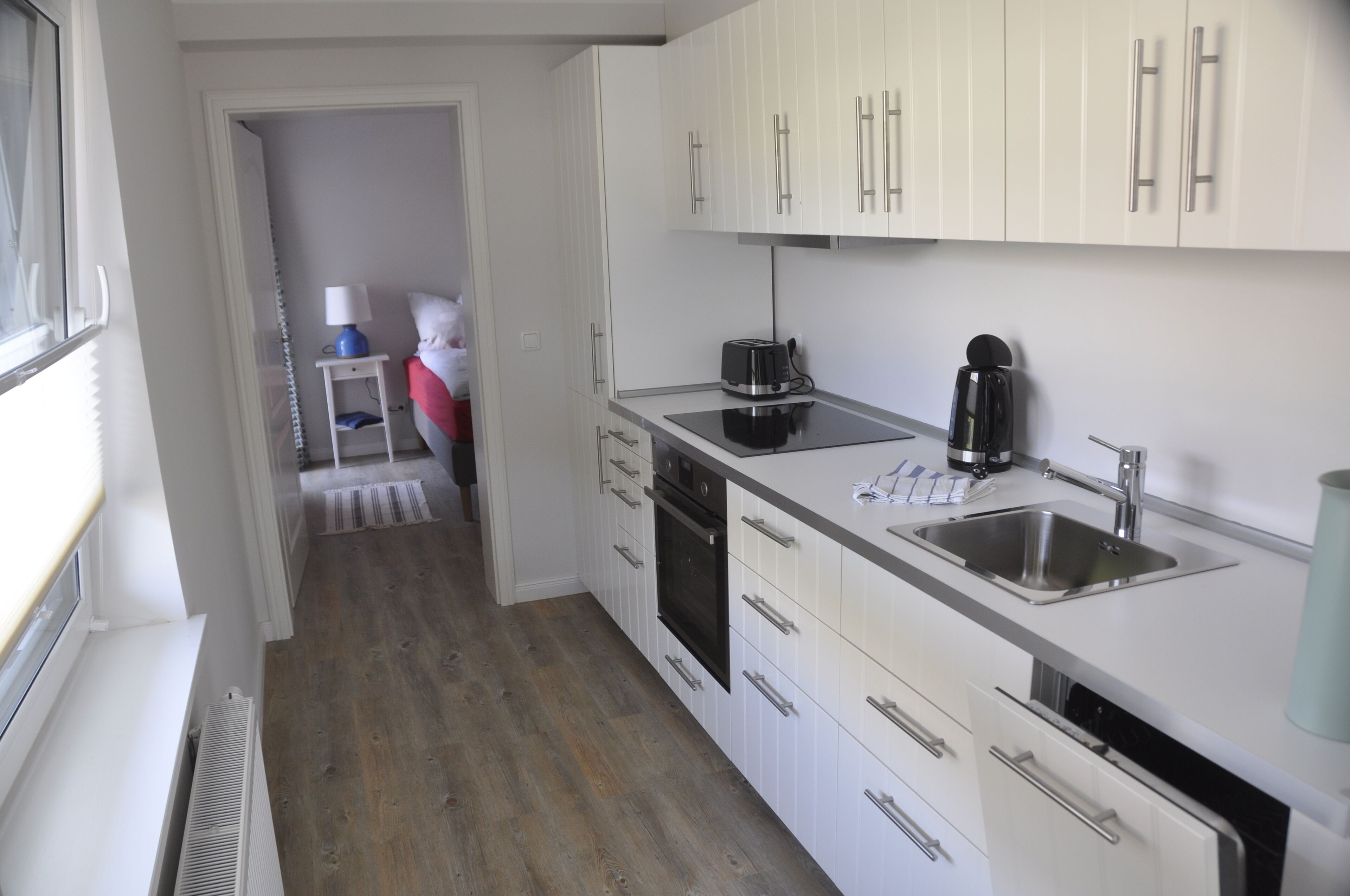 Una cocina moderna con armarios blancos, horno empotrado, cafetera y pileta.