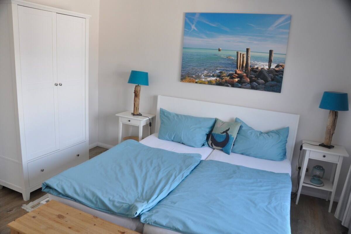 Une chambre à coucher comprenant un lit, deux tables de chevet, une armoire et un tableau représentant une scène de plage.