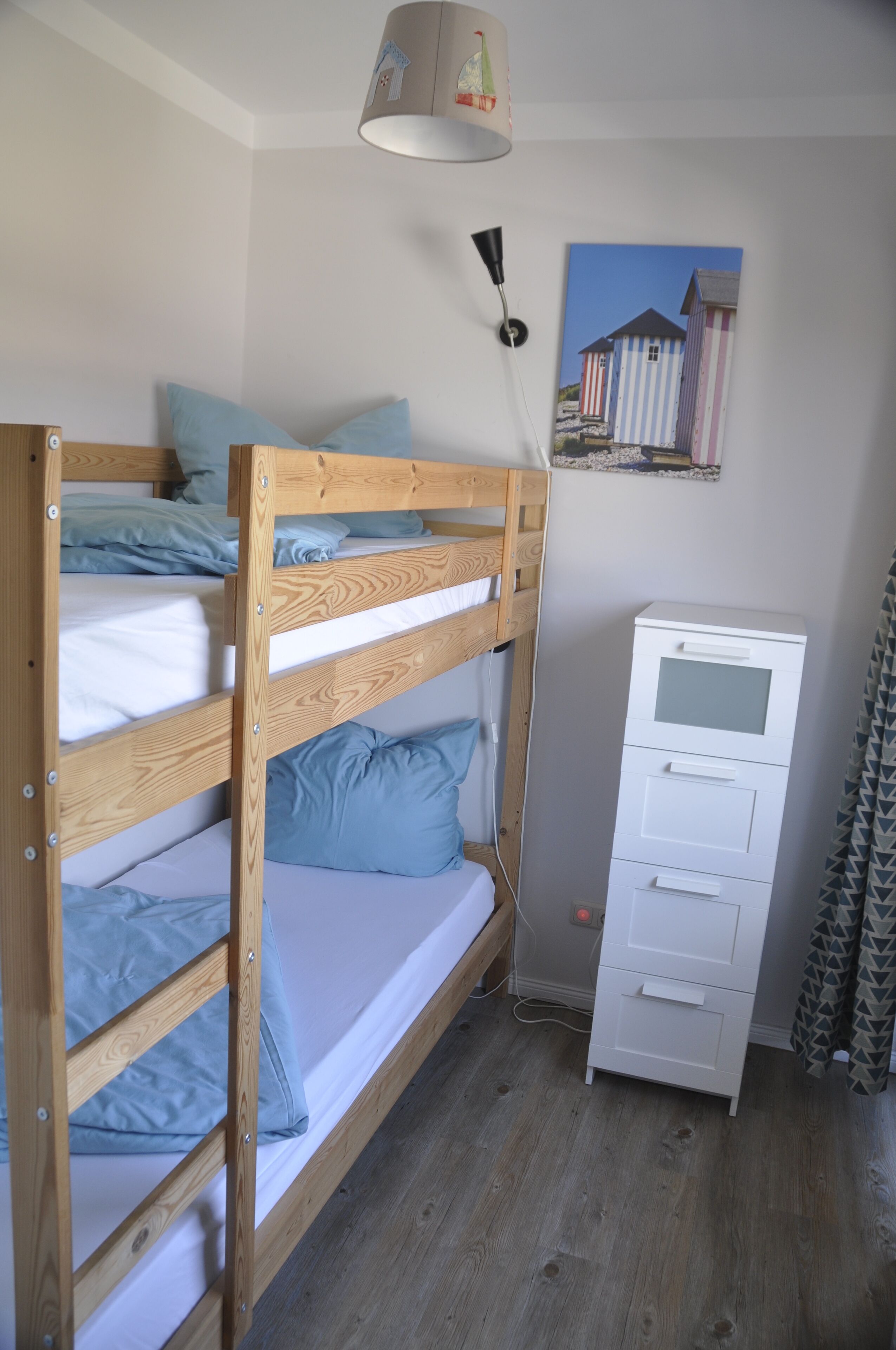 A bunk bed with blue bedding, a white dresser, and a wall-mounted lamp.