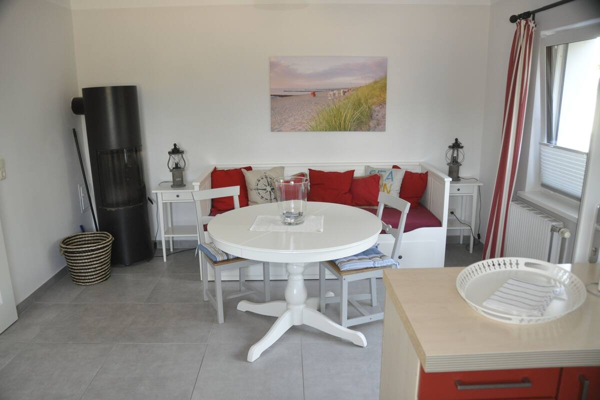 Une pièce avec une table ronde blanche, un canapé rouge et blanc, et un tableau représentant une scène de plage.