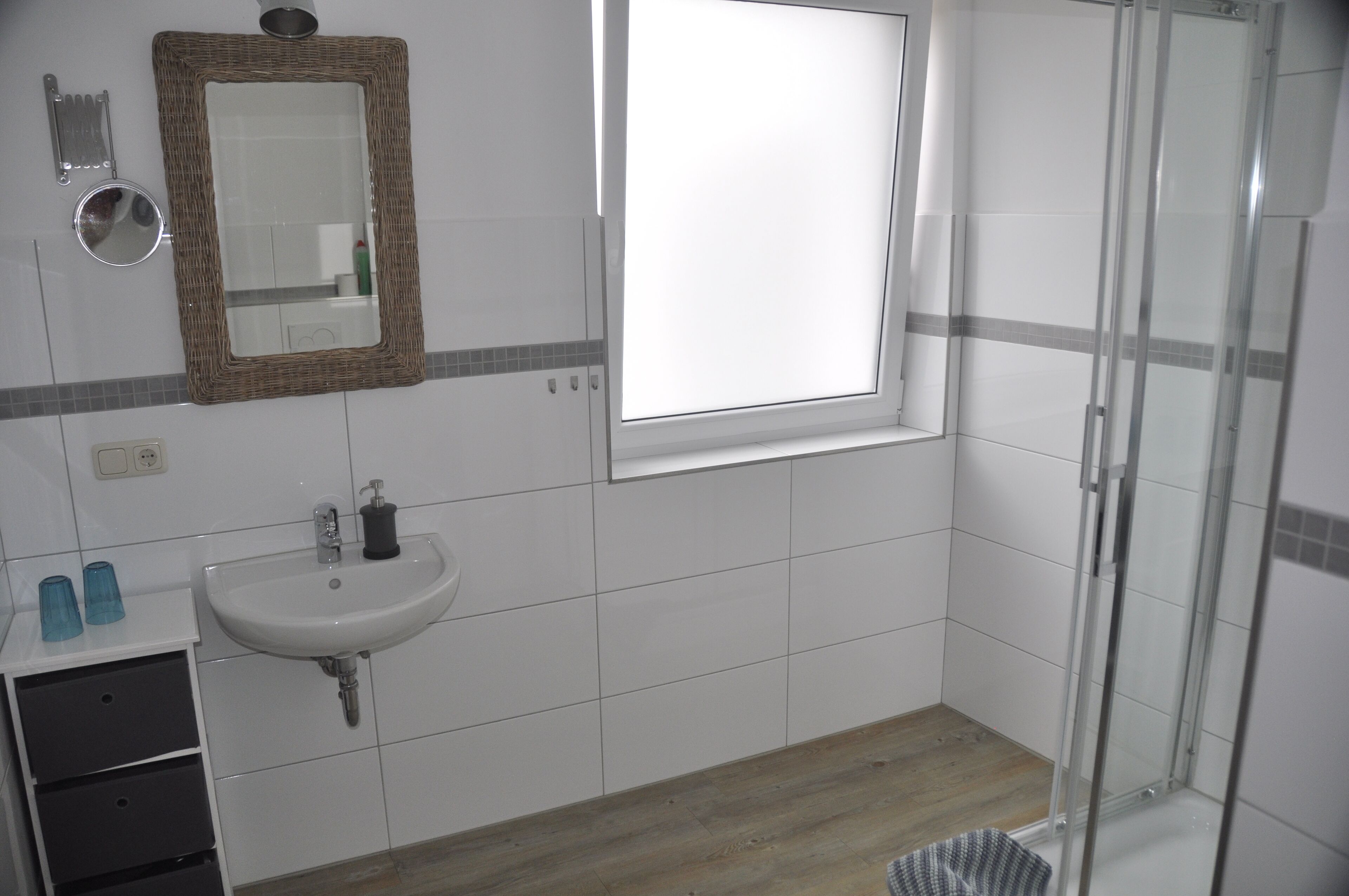 Une salle de bain avec un lavabo blanc, un miroir, une fenêtre et une cabine de douche en verre.