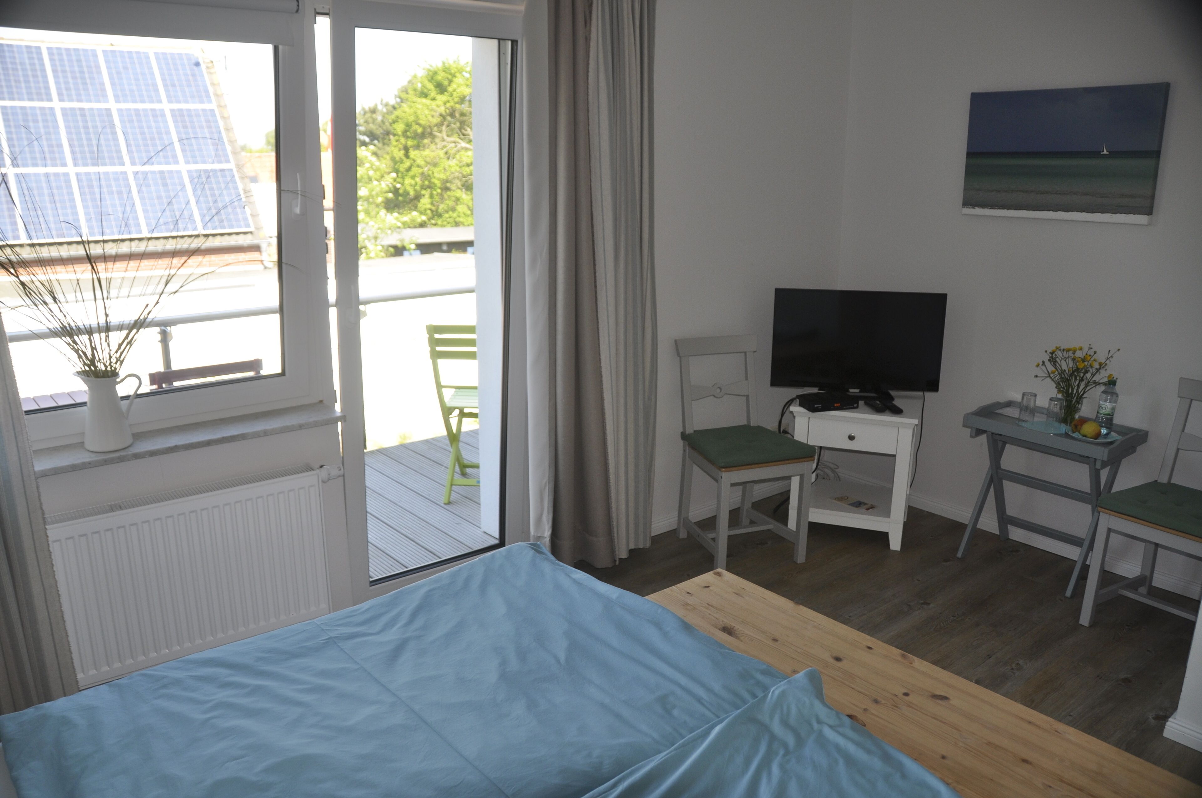 Una habitación con cama, un escritorio con televisor, una silla y ventana con vistas a paneles solares y vegetación.