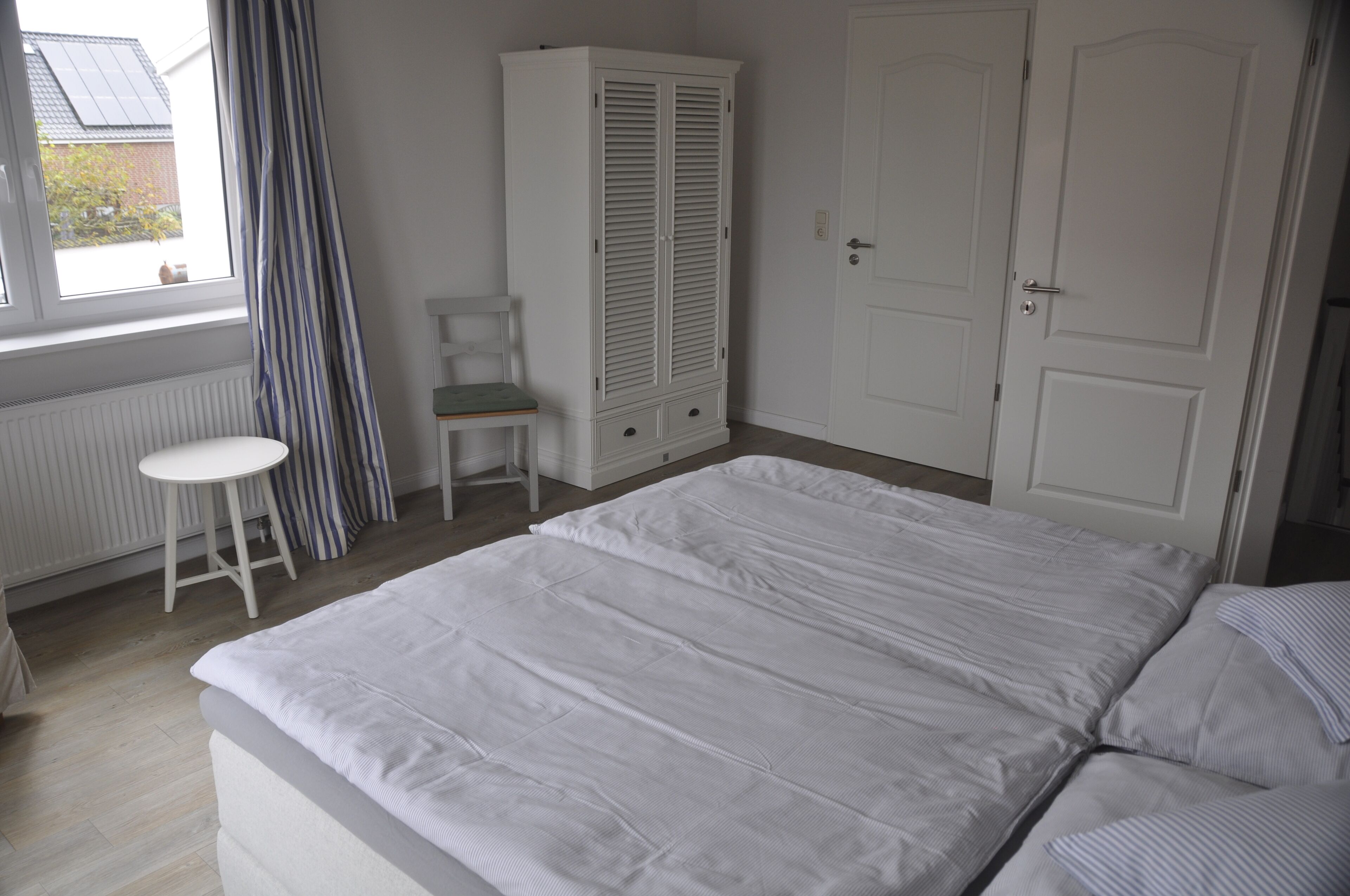 Een slaapkamer met een bed, een stoel, een kledingkast en een deur.