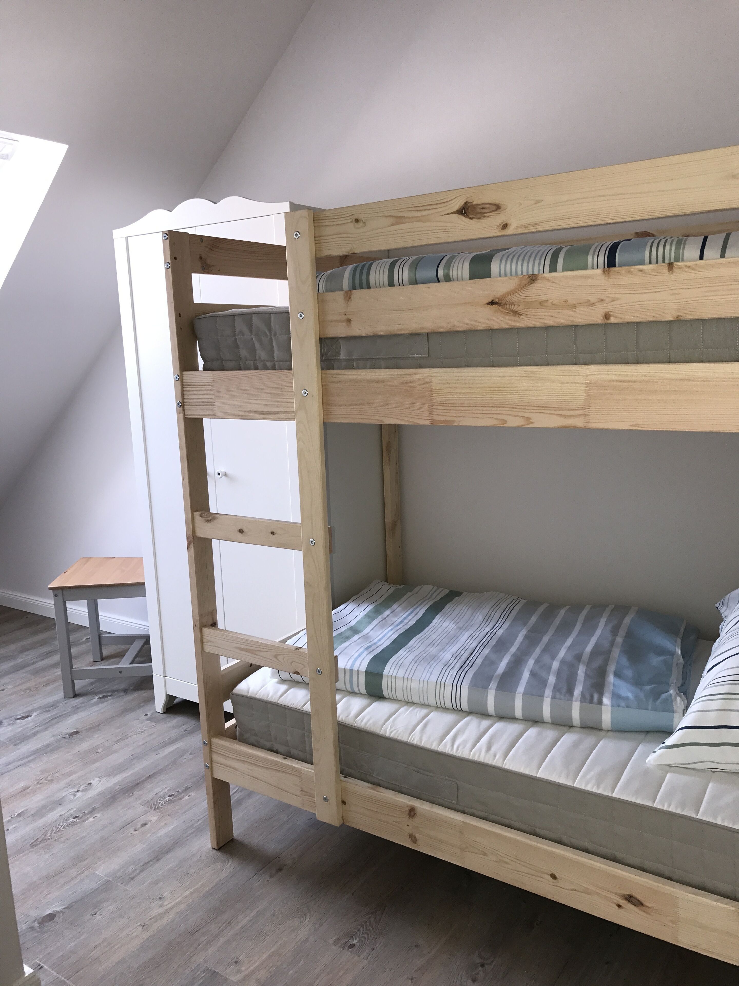 A bunk bed with a ladder, a small table, and a view of the sky through a window.