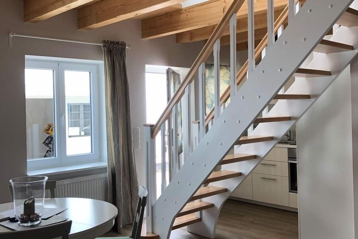Une cuisine moderne avec un escalier en bois, un coin repas avec une table et des chaises, et une fenêtre avec des rideaux.