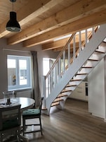 Eine moderne Küche mit einer Holztreppe, einem Essbereich mit Tisch und Stühlen sowie einem Fenster mit Vorhängen.
