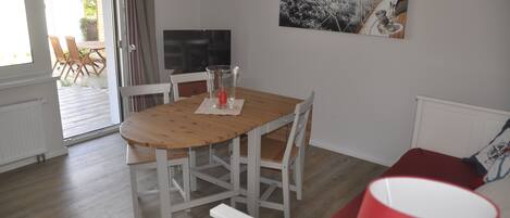 A dining area with a wooden table and white chairs, a glass of water, and a painting of a ship on the wall.