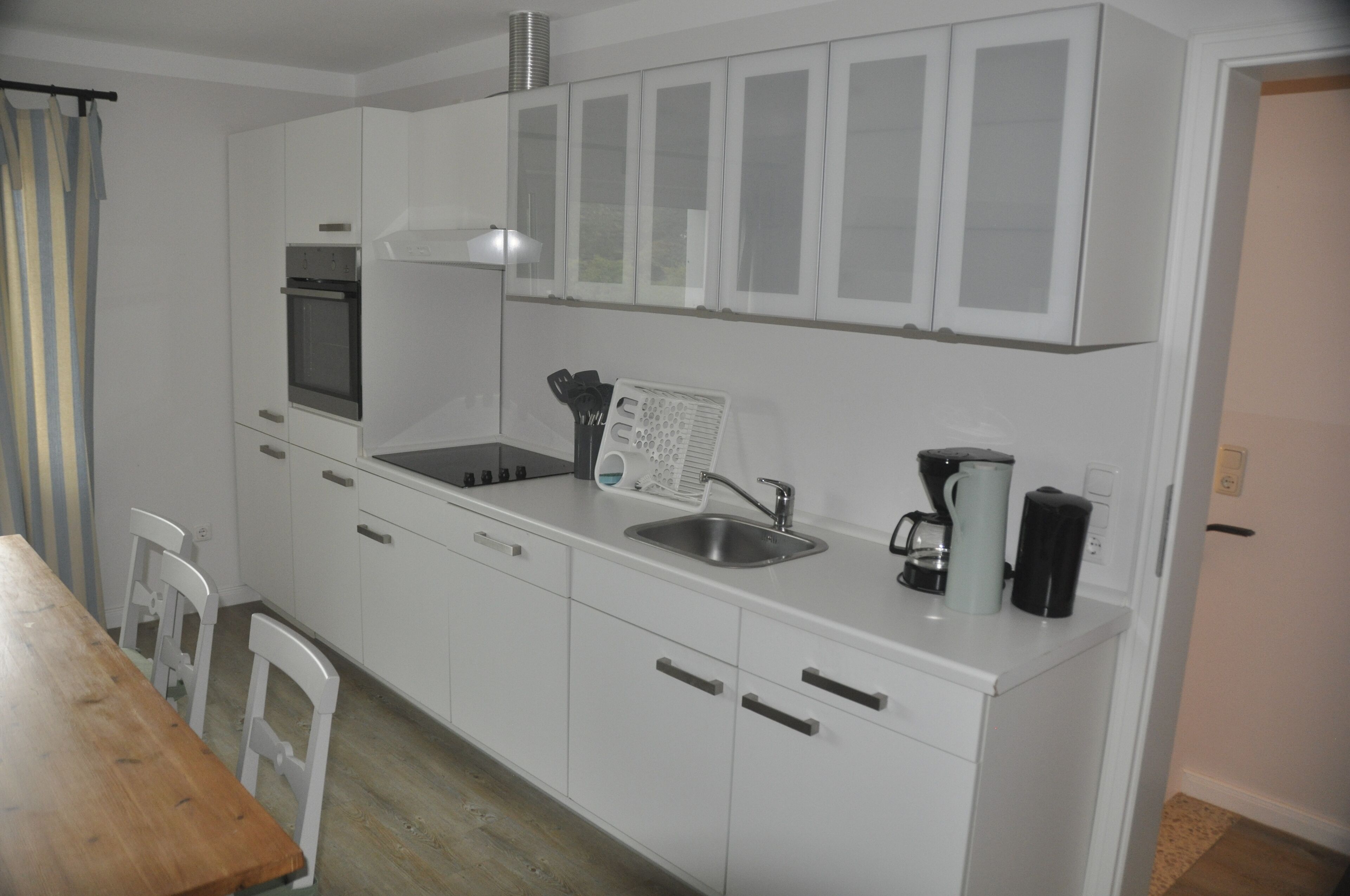 Eine kompakte Küche mit weißen Schränken, einem Backofen, einer Spüle und einer Kaffeemaschine.