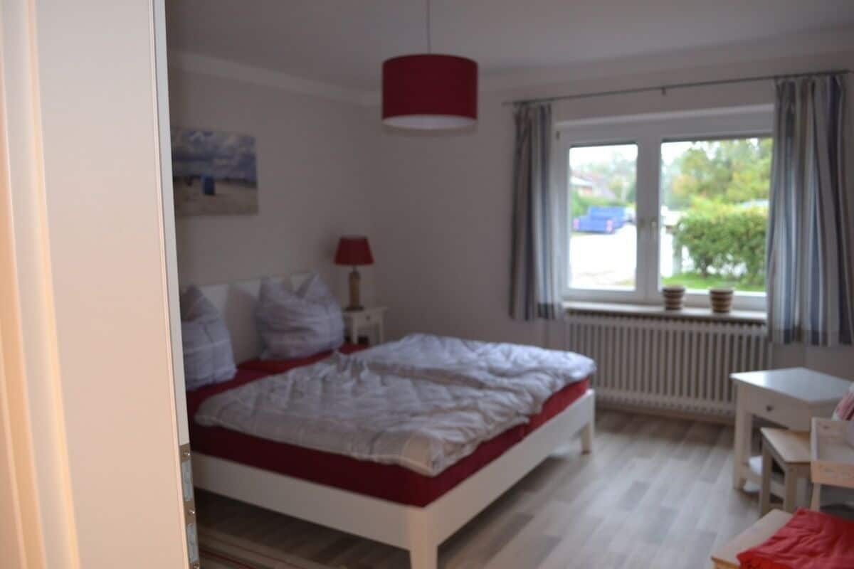 Une chambre à coucher avec un lit, un bureau, une lampe et une fenêtre avec des rideaux.