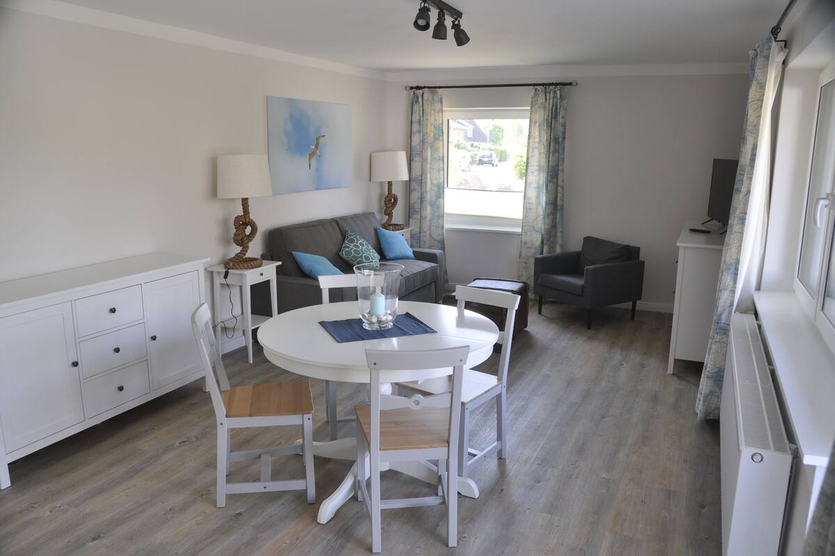 Un espace de vie compact comprenant une table à manger, deux chaises, un canapé, un téléviseur et une fenêtre avec des rideaux.
