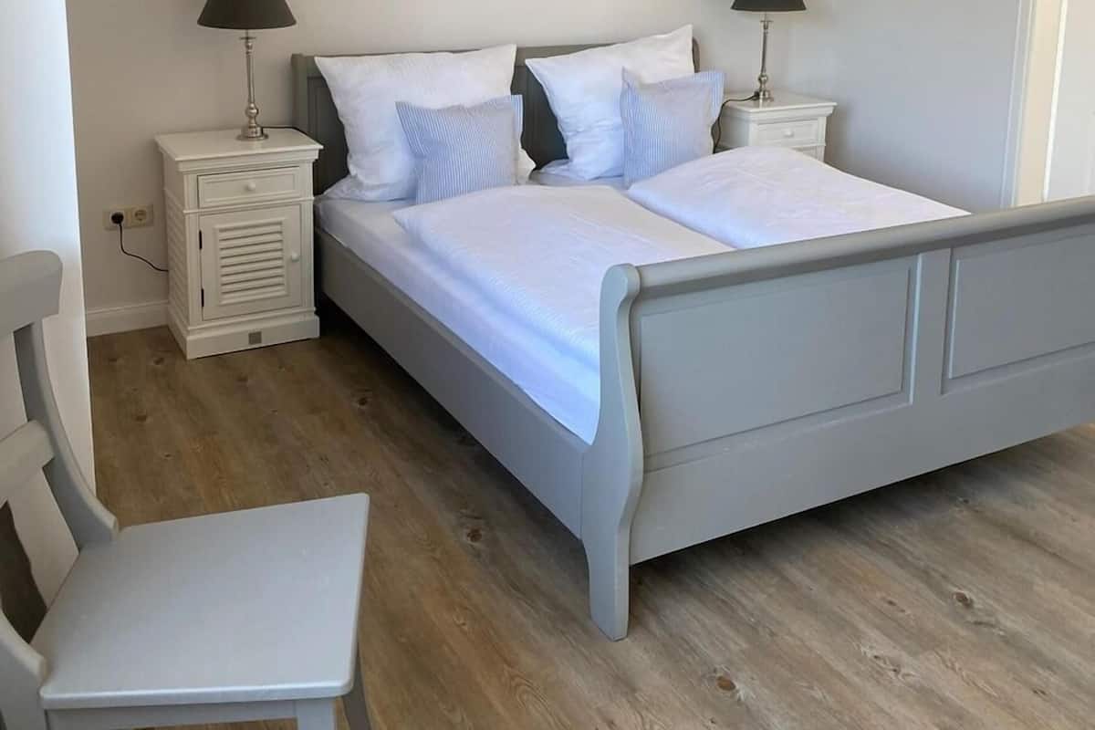 Une chambre à coucher avec un lit, deux tables de chevet avec des lampes, une chaise et un plancher en bois.
