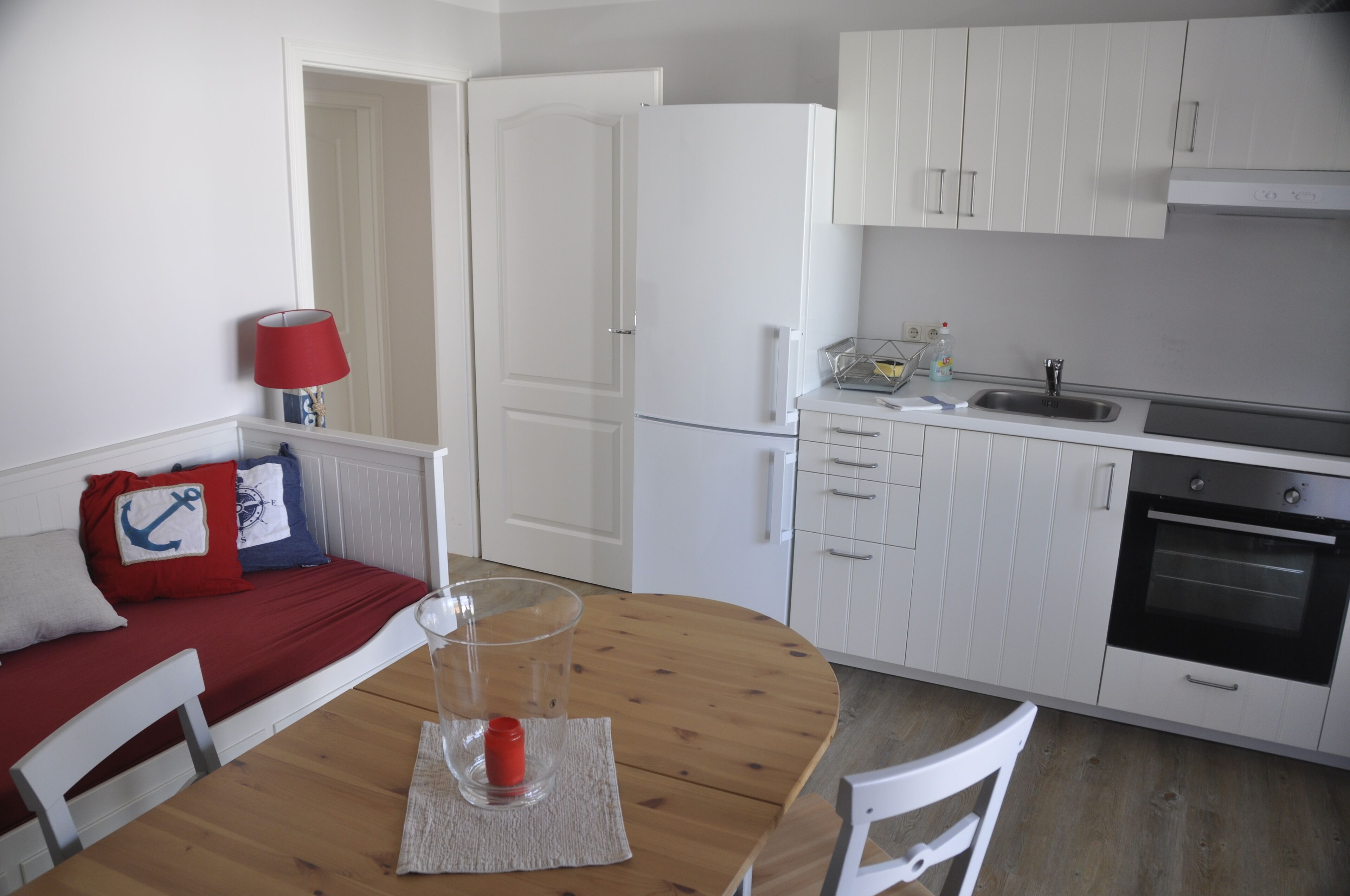 A compact kitchen with white cabinets, a built-in oven, and a dining area with a wooden table and chairs.