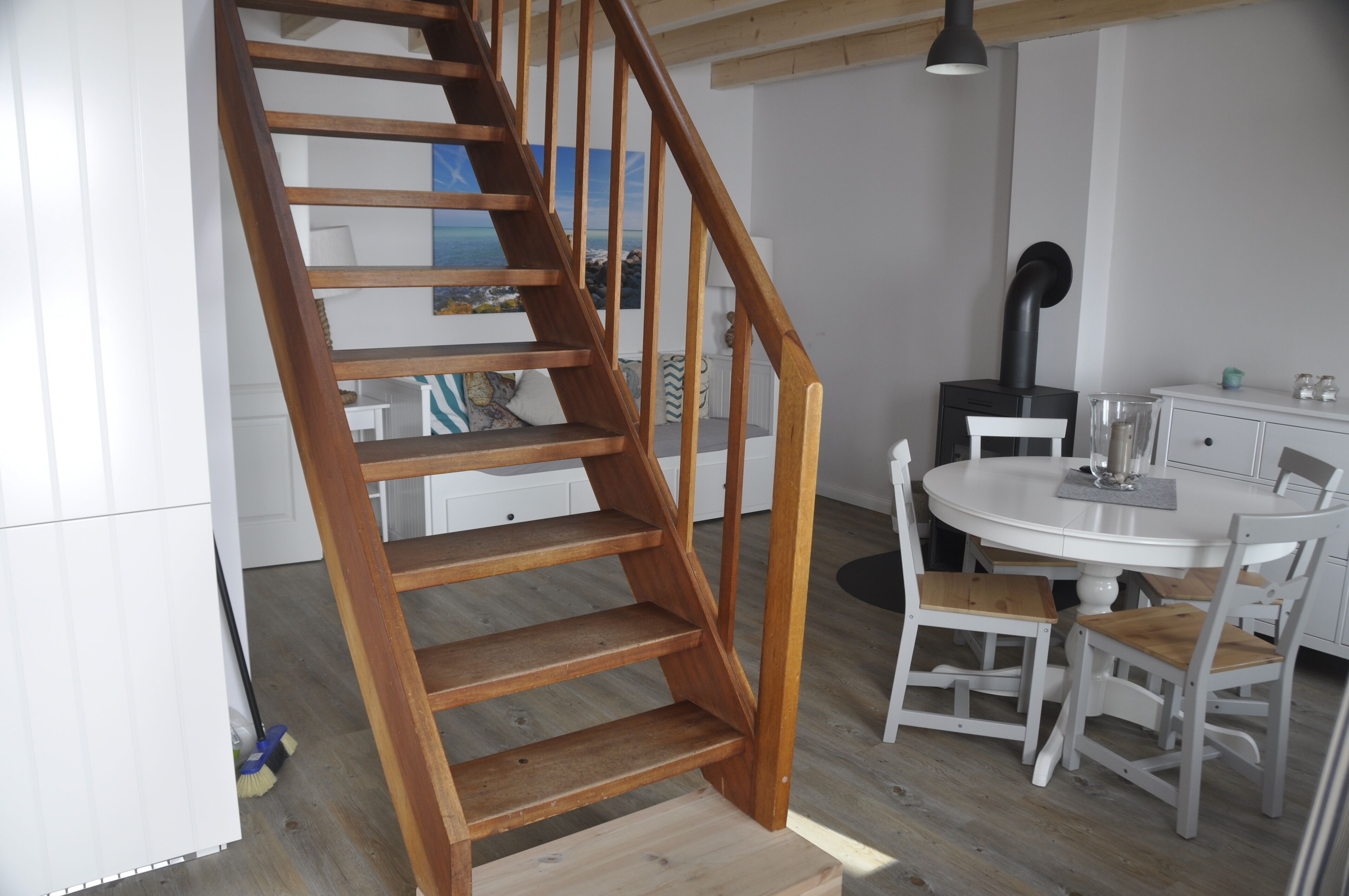 Un escalier en bois mène à un espace repas où se trouve une table ronde et des chaises blanches.