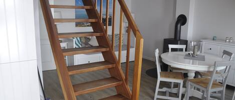 Un escalier en bois mène à un espace repas où se trouve une table ronde et des chaises blanches.