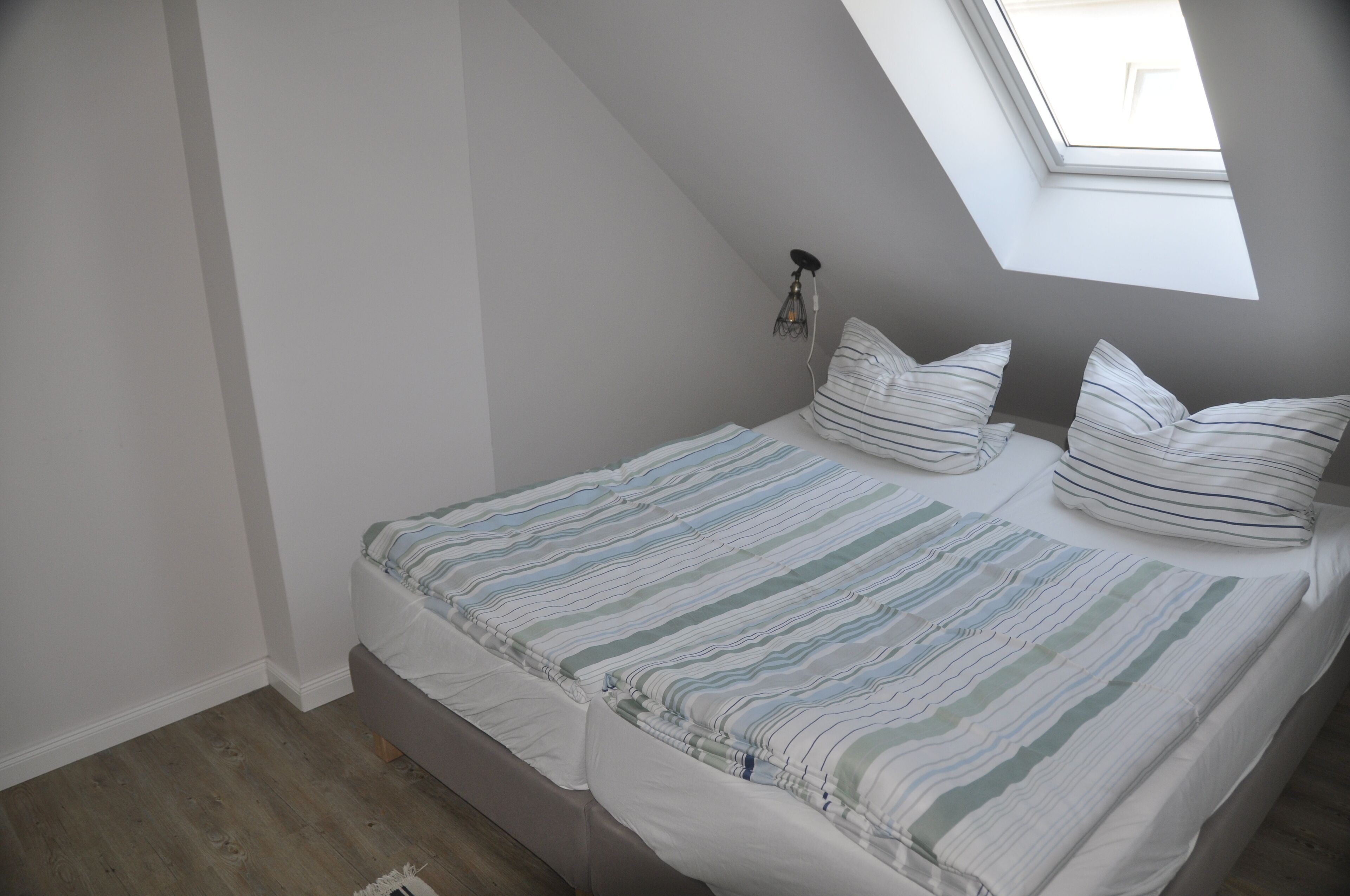 Quarto com teto inclinado e claraboia, com uma cama e roupa de cama listrada e duas almofadas.