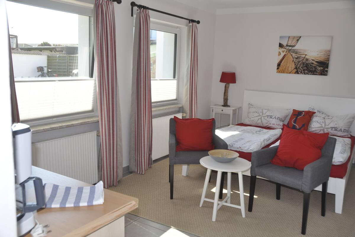 Une pièce comprenant un lit, deux chaises, une petite table, une lampe et une fenêtre avec des rideaux.