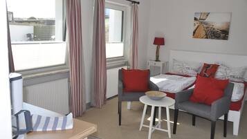 A room with a bed, two chairs, a small table, a lamp, and a window with curtains.