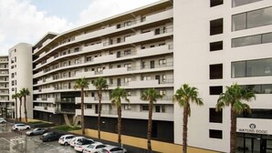 A multi-story hotel with a modern design, featuring a parking lot with several cars and palm trees in front. - Waters Edge 317 (Cape Town)