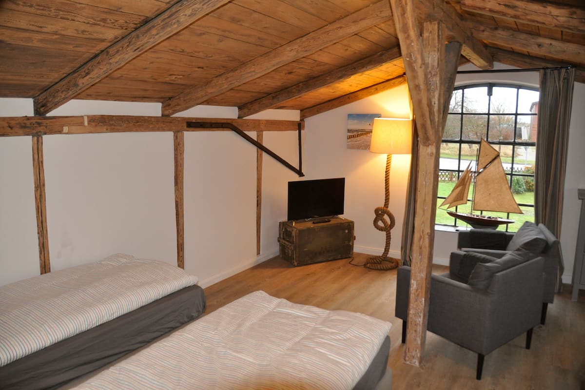Une chambre mansardée accueillante, avec un lit, une télévision, une lampe et une vue sur l’extérieur.