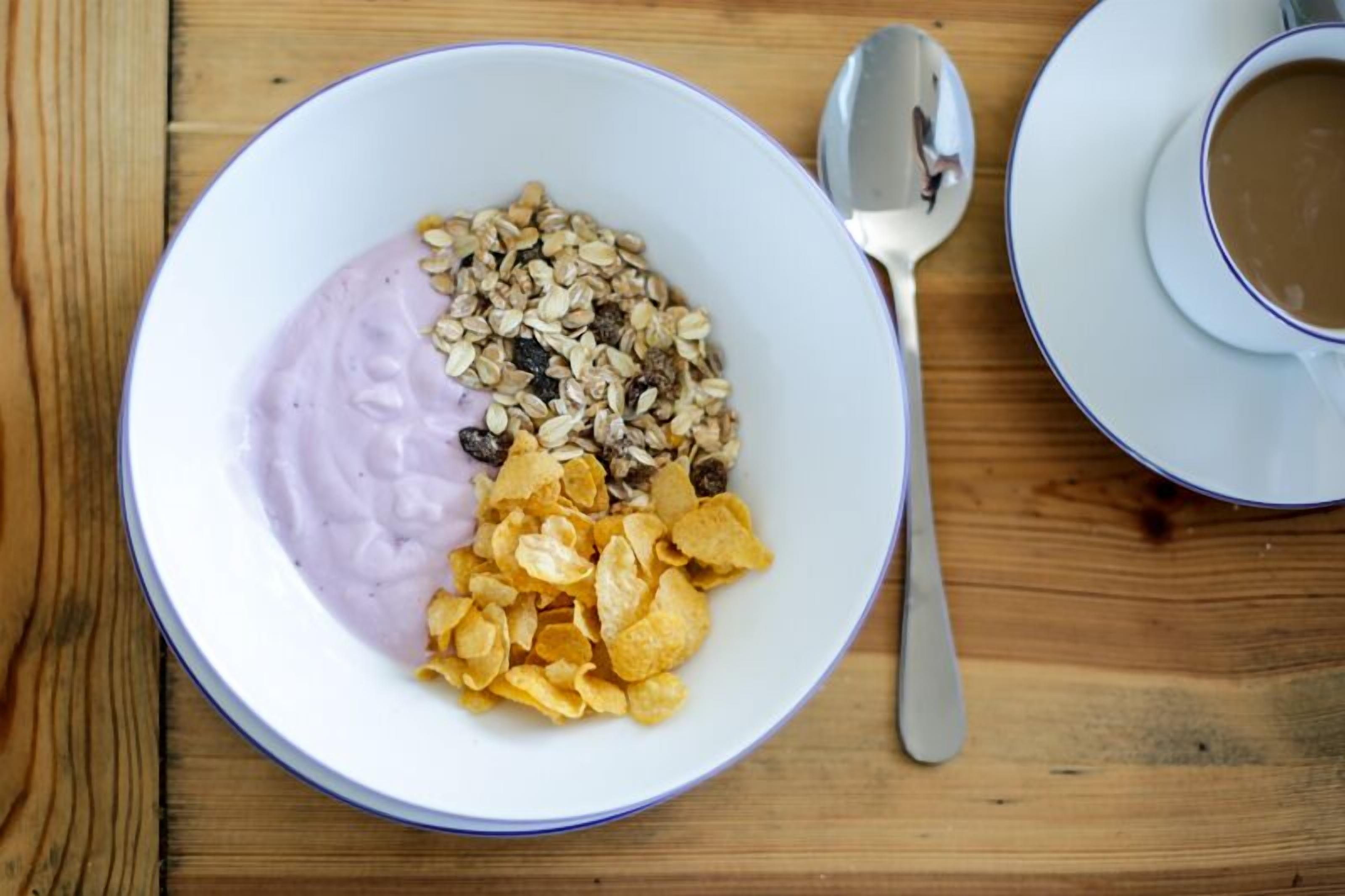 A bowl of yogurt with granola and cereal flakes on a wooden table.