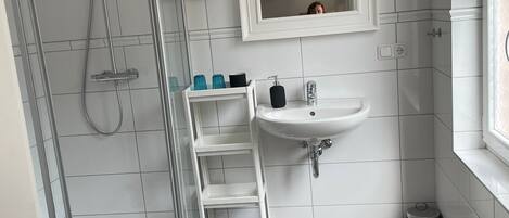 Ein modernes Badezimmer mit einer Duschkabine aus Glas, einem weißen Waschbecken und einem Spiegel darüber.
