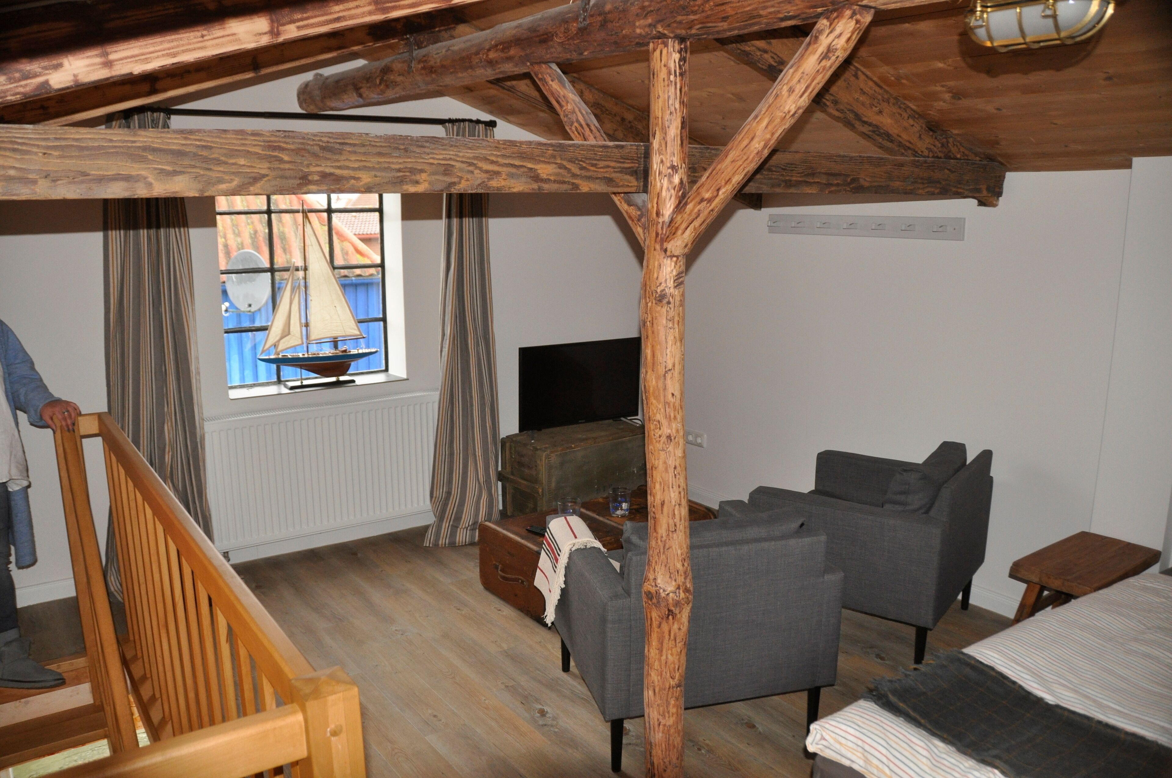 A room with a wooden ceiling, a sofa, a television, and a window with curtains.