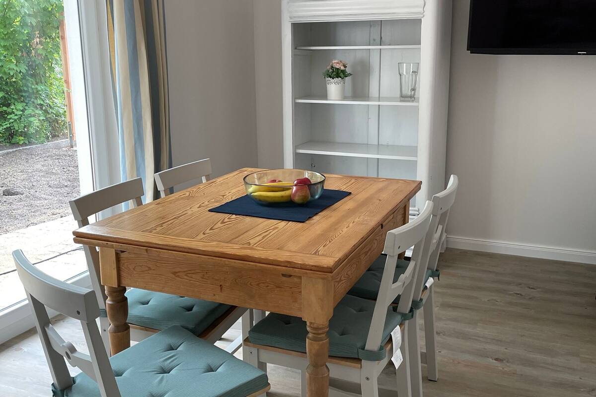 Un coin repas avec une table en bois, des chaises rembourrées de couleur turquoise, un meuble blanc et un téléviseur fixé au mur.