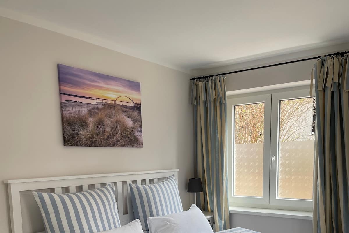 Un lit avec une literie à rayures, une table de chevet, une lampe et une fenêtre avec des rideaux.