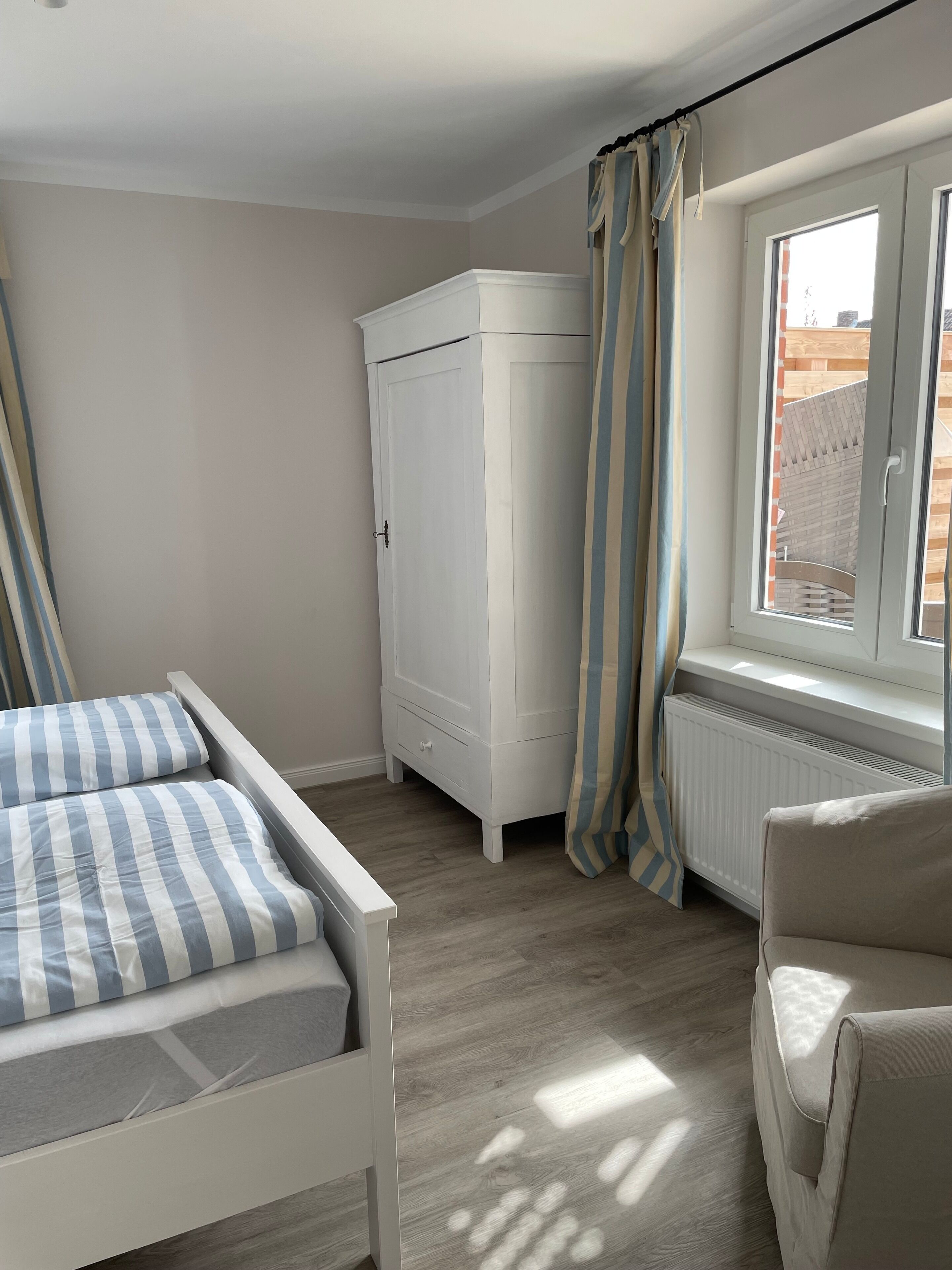 Ein Schlafzimmer mit Bett, Kleiderschrank, Heizkörper und einem Fenster mit Vorhängen.