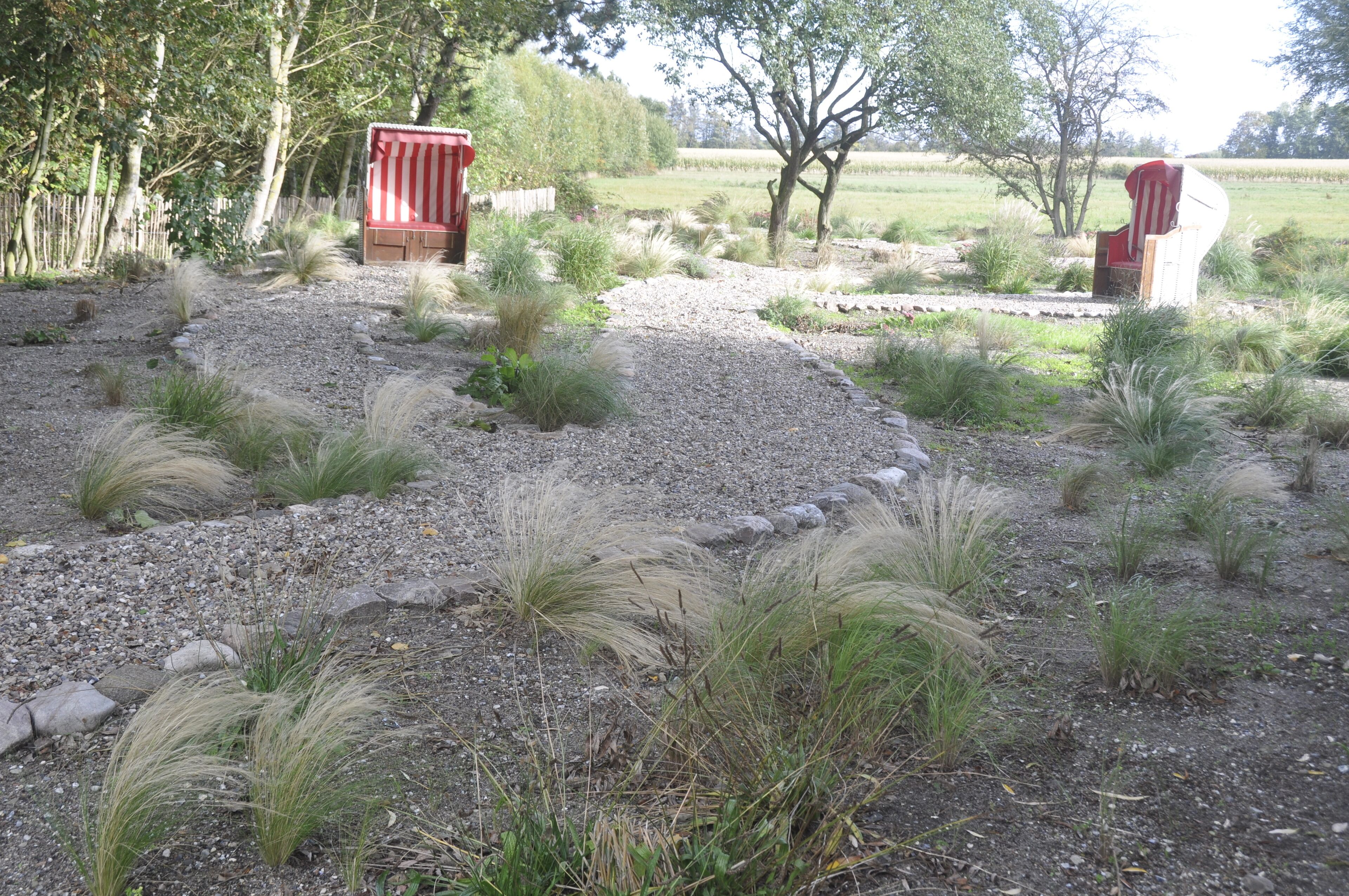 Een tuin met een grindpad, kleine struiken en twee gestreepte constructies in rood en wit.