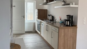 Une cuisine moderne avec des meubles en bois, un four encastré, une machine à café et une fenêtre à vitrage dépoli.
