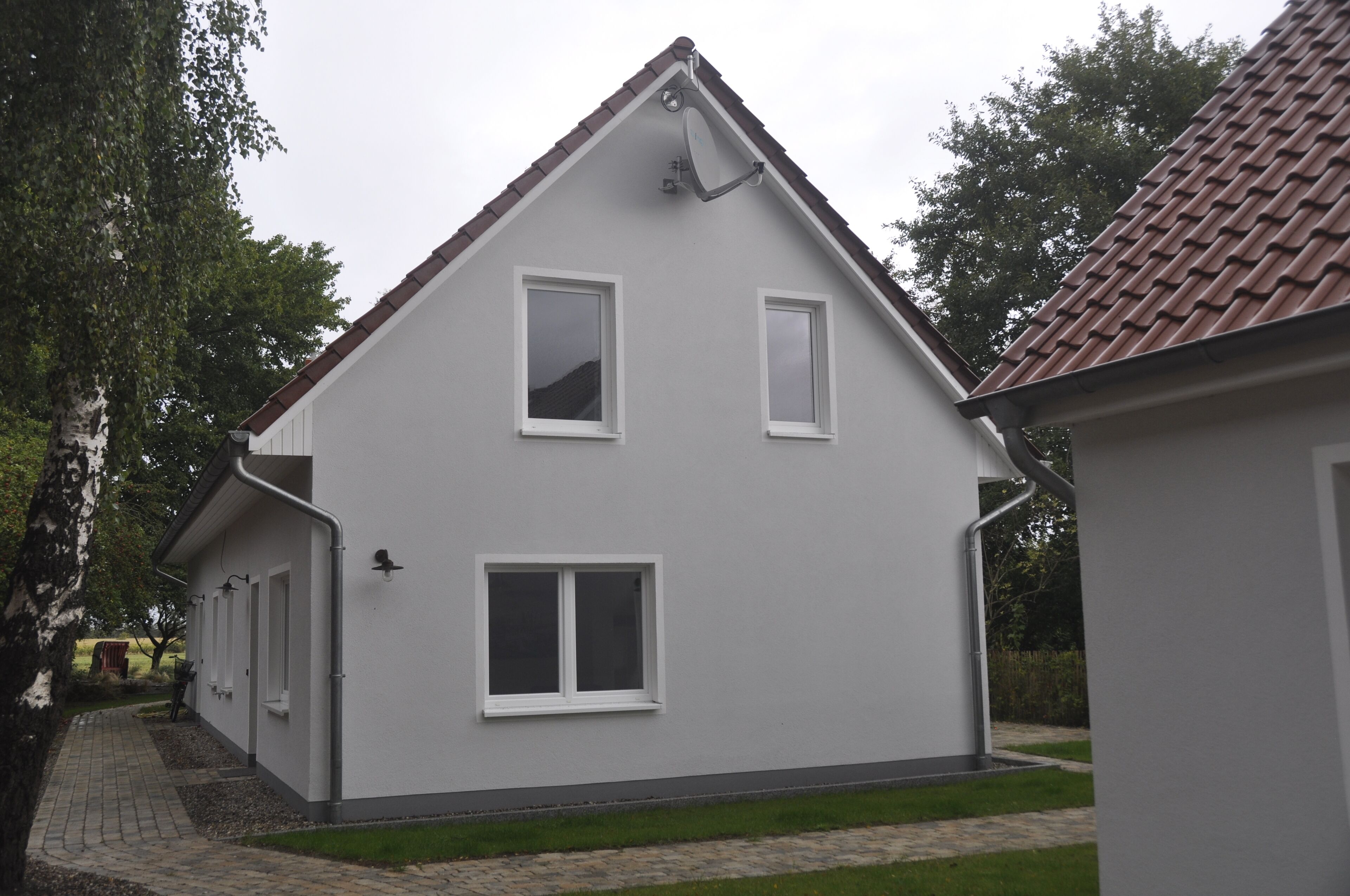 A two-story house with a sloped roof, white exterior walls, and a paved driveway.