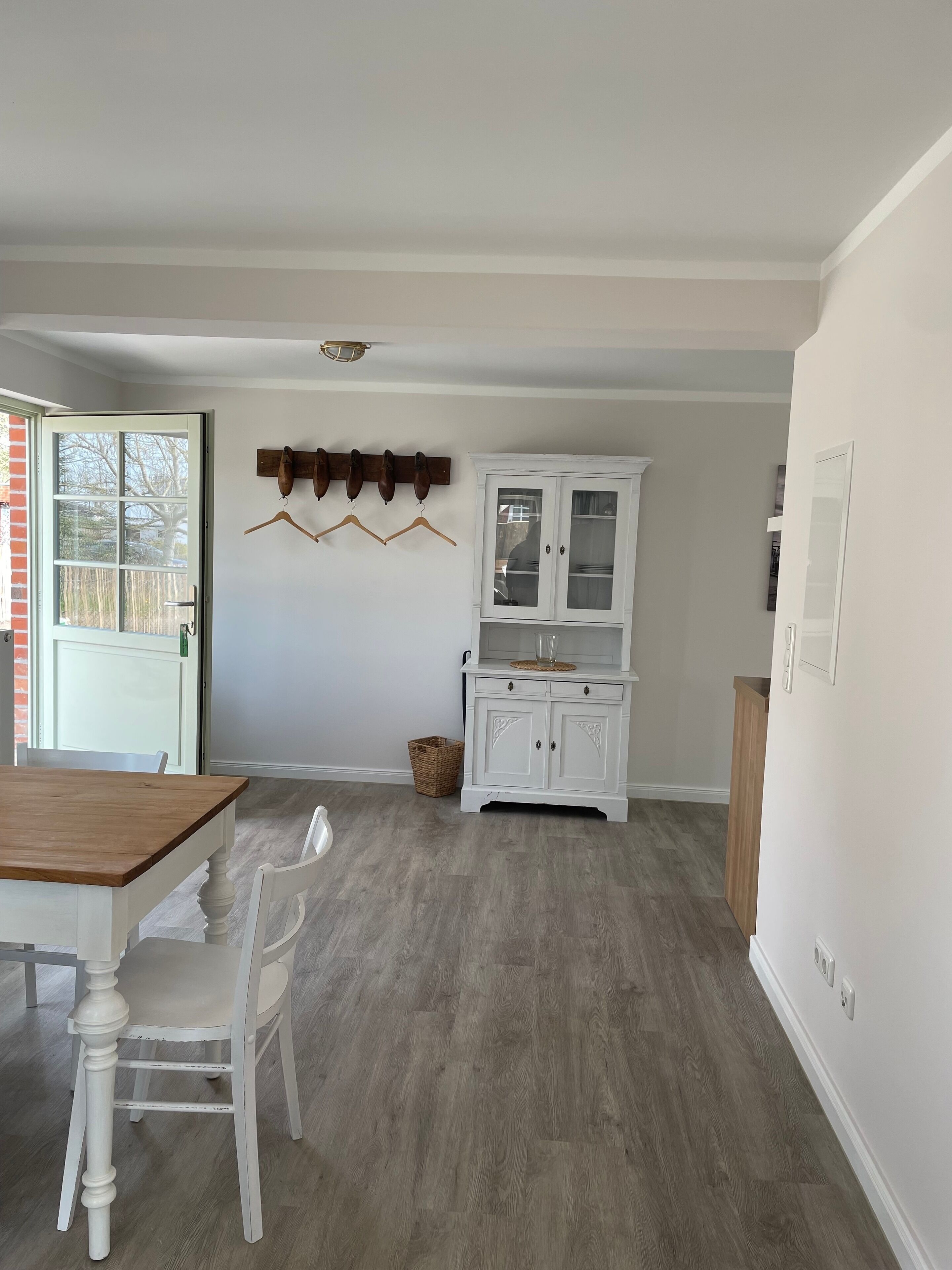 A kitchen with a wooden table and chairs, a white cabinet, and a hanging wooden rack.