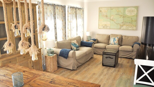 Un salon chaleureux avec un plancher en bois, un ensemble de canapés, une carte accrochée au mur et un luminaire suspendu.