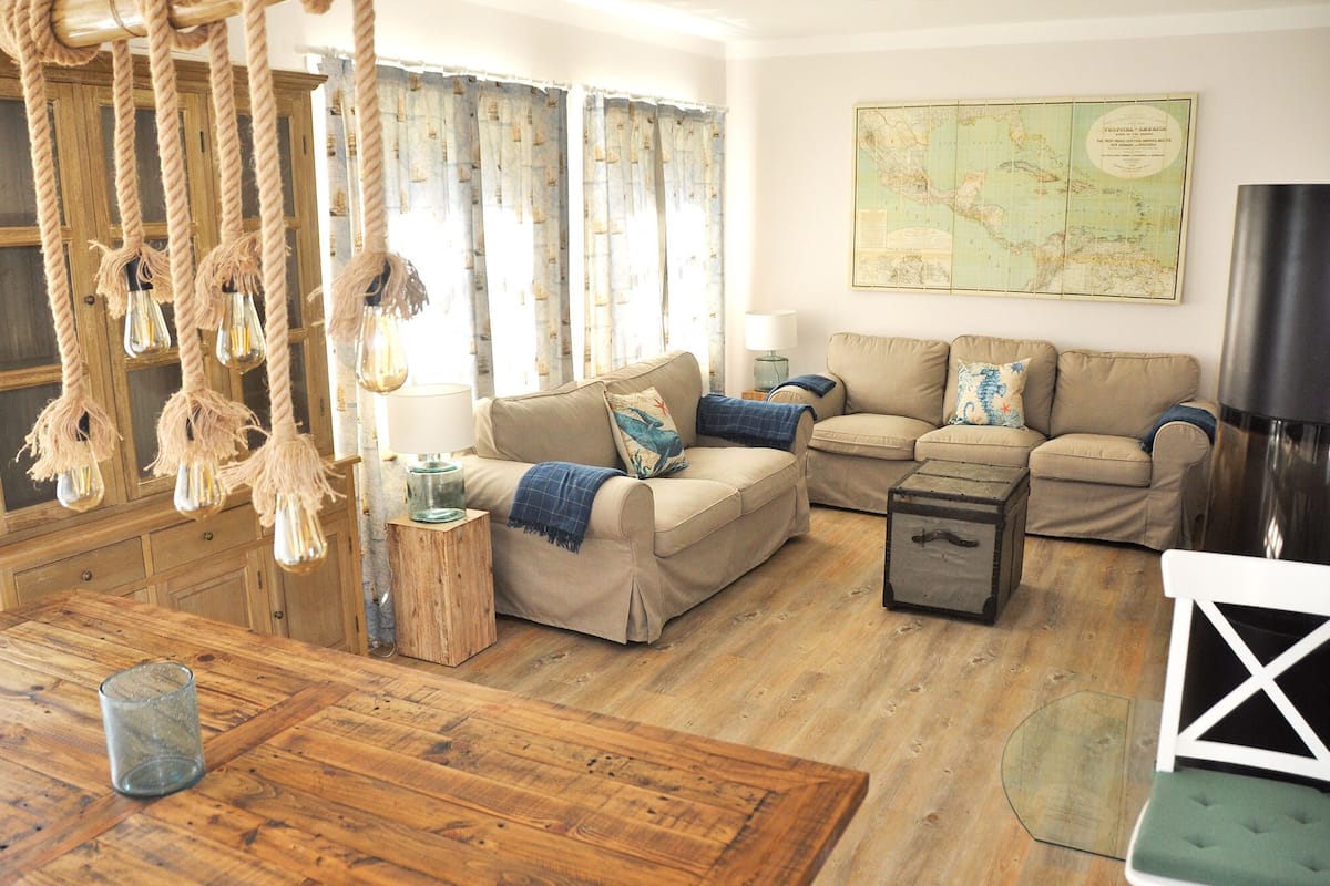 Un salon chaleureux avec un plancher en bois, un ensemble de canapés, une carte accrochée au mur et un luminaire suspendu.