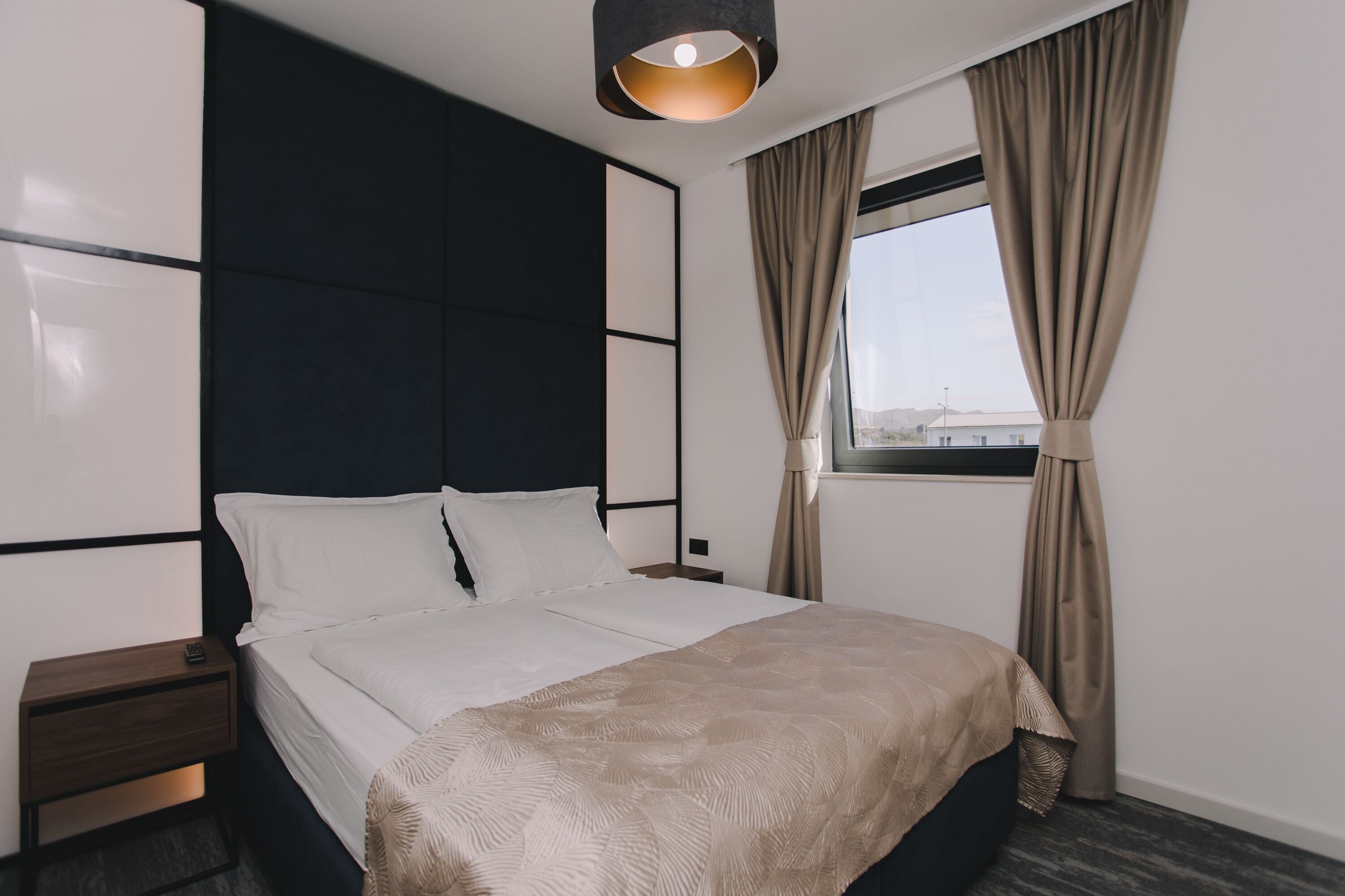 A modern hotel room with a large bed, a bedside table, a nightstand, and a window with curtains.