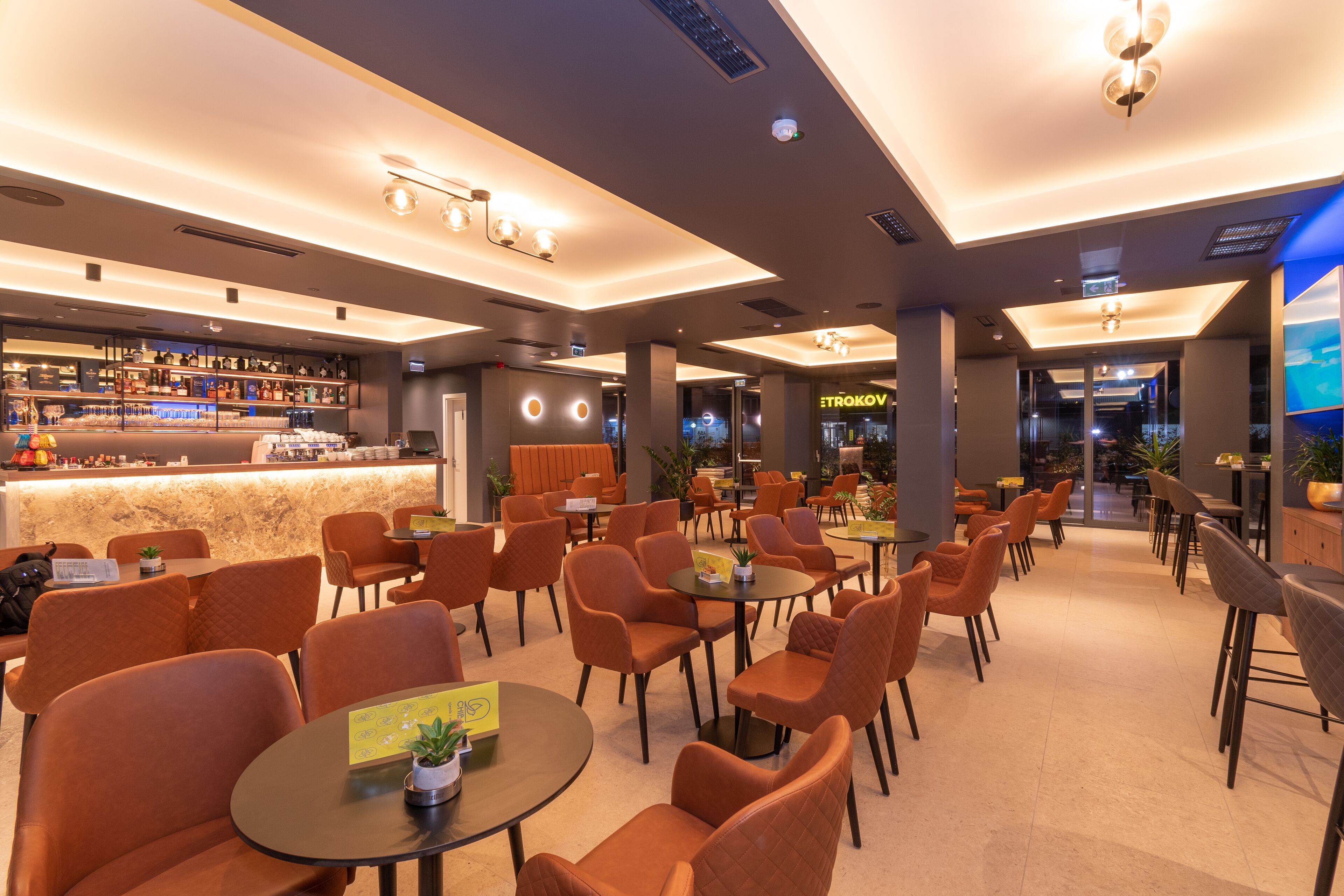 Un espace intérieur moderne comprenant un bar, des coins salon et un magasin visible appelé « METROKOV ».