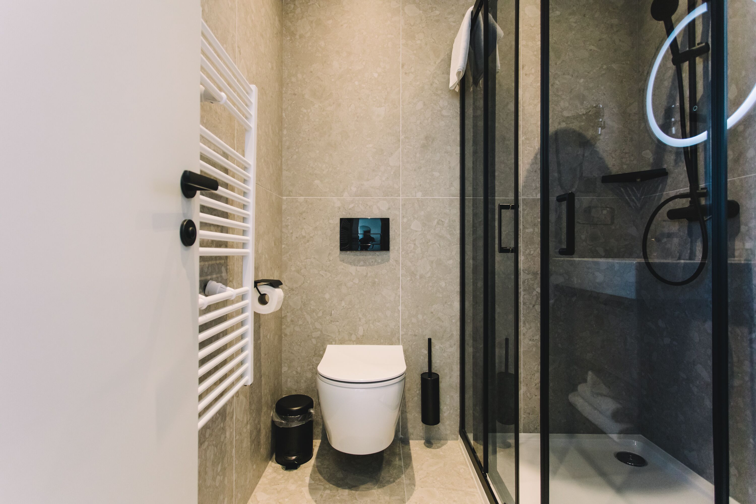 Et moderne badeværelse med brusekabine i glas, et hvidt toilet og en håndklædestang.