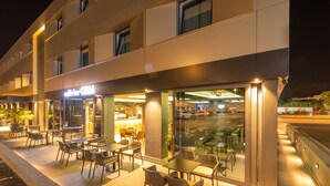 Un espace extérieur aménagé avec des tables et des chaises, une entrée avec une porte vitrée et une vue sur la rue.