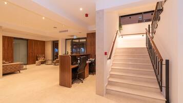 A spacious living area with a wooden desk, comfortable seating, and a staircase with a modern railing.